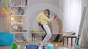 Wide shot portrait of confident carefree young woman imitating guitar playing on broom cleaning house. Joyful happy