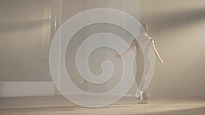 Wide shot portrait of graceful slim ballerina rehearsing performance in front of mirror in dancing studio backlit fog