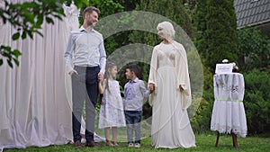 Wide shot portrait of happy interracial newlyweds posing with children at wedding altar in spring garden. Smiling