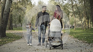 Wide shot portrait of happy young Caucasian family strolling along park alley and talking. Positive handsome father