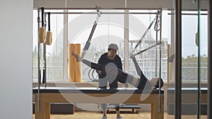 Wide shot portrait of professional personal trainer helping Caucasian sportswoman with pilates exercising. Serious