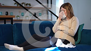Wide shot portrait of sad pregnant woman crying sitting on couch in living room at home. Upset Caucasian beautiful young