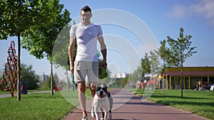 Wide shot portrait of satisfied relaxed Caucasian man walking with dog on sunny park alley leaving. Happy confident
