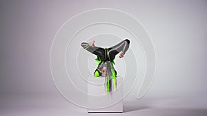 Wide shot portrait of slim flexible woman emerging behind cube at white background doing back walkover posing. Fit