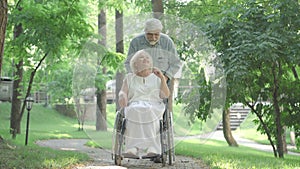 Wide shot portrait of smiling senior disabled woman in wheelchair enjoying sunny summer day in park with loving husband