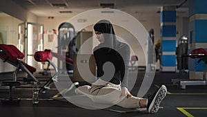 Wide shot serious slim fit sportswoman in hijab stretching leg muscles sitting on twine raising leg with hand. Portrait
