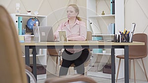 Wide shot of serious woman working with laptop in office and rubbing neck. Portrait of concentrated mid-adult lady