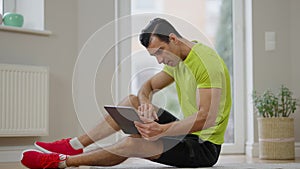 Wide shot side view of concentrated handsome Middle Eastern man sitting indoors using tablet with snow falling outdoors