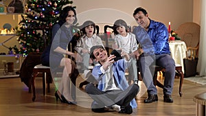 Wide shot smiling teenage boy recoding family video on camera with family sitting at background on New Year's eve. Happy