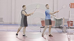 Wide shot of sportsmen training badminton hand movement indoors. Portrait of positive Caucasian men training sport game