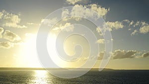 Wide shot of a sunset in timelapse over the ocean and cliffs on the horizon. Zooming progressively on the cliffs.