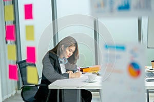 Wide shot through transparent board pretty young business woman use pen to write and note on paper in office and she look