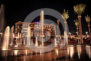 Wide shot of tropical trees and ground water fountains near Emirates Palace at night in Abu Dhabi