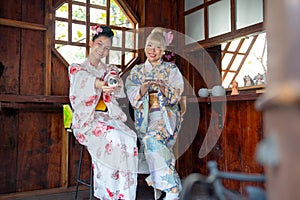 Wide shot of two Asian women wear japanese style dress sit and enjoy in small shop and also hold small gift and look to camera