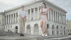 Wide shot of two cheerful girls dancing simultaneously in city. Portrait of beautiful Caucasian young women enjoying