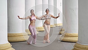 Wide shot two talented dancers moving simultaneously shaking body performing Indian dance outdoors. Slim flexible women