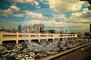 Wide shot of vehicles parked in a parking lot near buildings under a cloudy blue sky