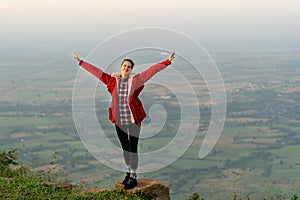 Wide shot of woman wear red coat and stand with spread her arms near cliff on the mountain and look at camera with beautiful high