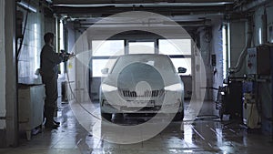 Wide shot of worker washing vehicle in car wash. Caucasian employee using high-pressure washer at service station