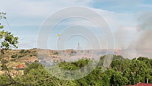 Wide shot yellow fire helicopter flying over smoke releasing water on fire on sunny summer day outdoors. Firefighters