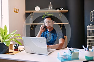 A wide shot of a young businessman taking a call at his desk in a trendy office