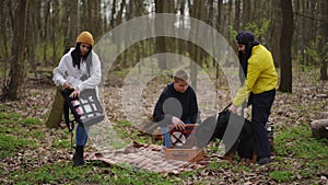 Wide shot young Caucasian man and women having picnic with dog outdoors. Carefree relaxed friends enjoying weekend