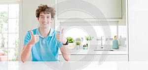 Wide shot of young handsome man at home success sign doing positive gesture with hand, thumbs up smiling and happy