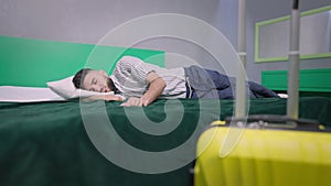 Wide shot of young handsome man sleeping on comfortable cozy bed with packed yellow travel bag at front. Brunette