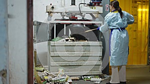 Wide shot young woman placing paper trash in hydraulic press machine. Positive confident Caucasian worker in uniform