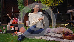 Wide shot of young woman sitting on blanket on backyard with cute little puppy running to owner. French Bulldog and