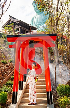 Wide shot of young woman wear japanese style dress also hold red umbrella stand on stair and look at camera with smiling in area