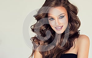Wide smile and tender look of young brown haired woman with voluminous, shiny hair. Perfect makeup and trendy hairstyle.