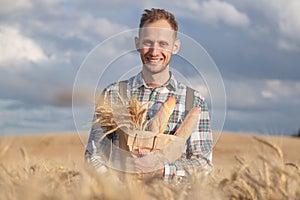 Wide smiling farmer or baker with baguettes in rye, wheat field