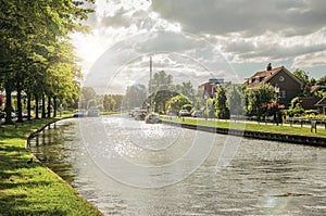 Wide tree-lined canal with houses and boats and shine of sunset reflected in water at Weesp.