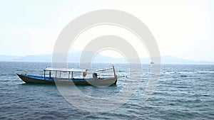 Wide view of the ambient hypnotic motion of an anchored traditional khmer boat on a calm sea