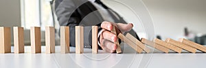 Business mediator stopping falling wooden dominos with his hand photo