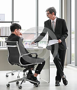 Wide view portrait shot of two Asian businessmen in the office. Senior leader pointing to the paper to show the mistake made by