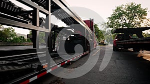 Wide view of Two trucks with a car hauler stand in the parking lot. Rear view, move camera