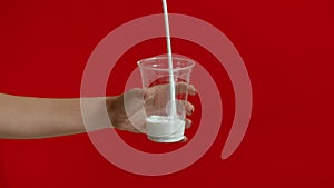 Wide view of woman hands pouring milk into empty plastic glass in slow motion.