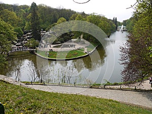 Wide water canal with fountain. Around it there are pairs with green flower beds, on one of which the number of flowers