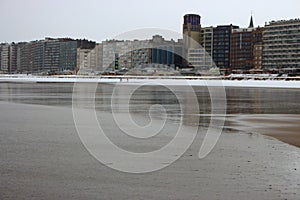 Wide winter beach with wet sand and snow and row of houses along seacoast on cloudy day. Modern architecture on coast.