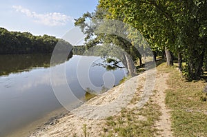 Wide yellow river is slow flowing. Early autumn. Sunny weather and brightgreen trees on the banks fron the both sides