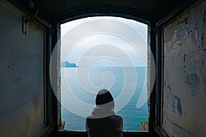 wideangle shot of a person gazing out to a calm blue sea from lighthouse window