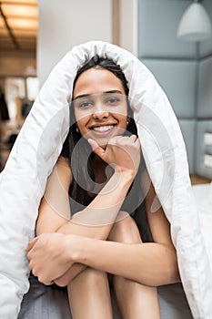 A wider view of a woman smiling while lying down the bed under the quilt