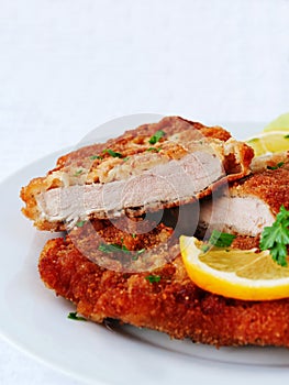 Wiener Schnitzel cut in two served with lemon slices and parsley leaves over white, vertical