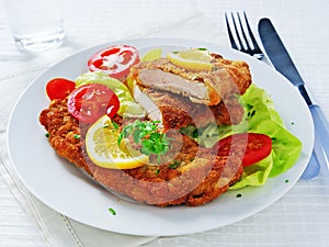 Wiener schnitzel over lettuce leaves with sliced tomatoes and lemon