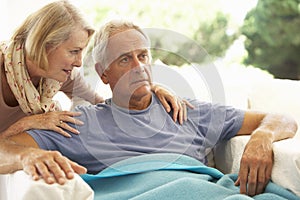 Wife Comforting Senior Man Feeling Unwell Resting Under Blanket