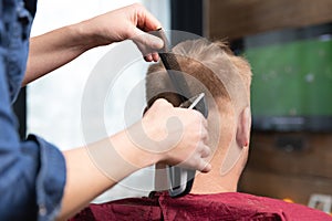 Wife cutting husbands hair at home in front of TV with clipper and holding comb in other hand. Haircut at home