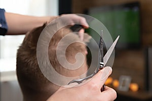 Wife cutting husbands hair at home in front of TV . Scissors in focus