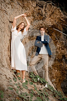 Wife with her hands raised up and her husband are standing near a steep cliff